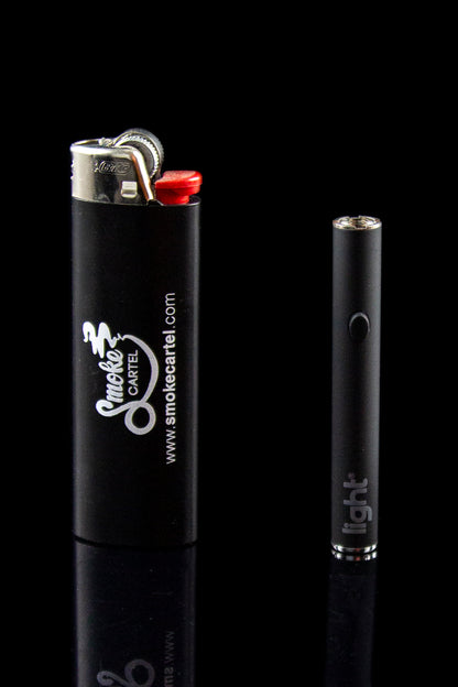 Black lighter with “Smoke Cartel” branding next to a clear glass tip, both reflected on a dark surface.
