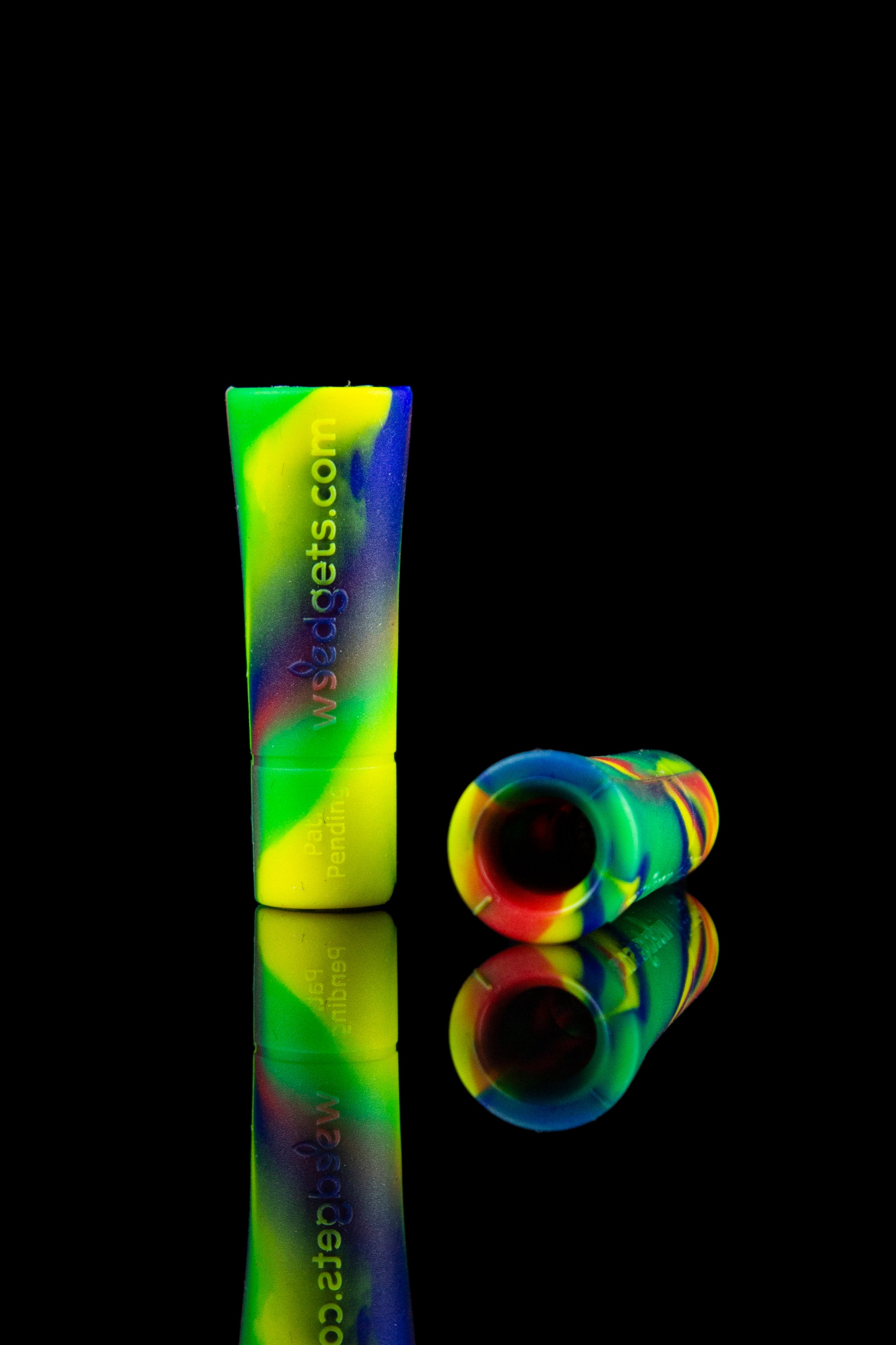 Colorful glass cannabis pipe and mouthpiece reflecting on a black surface.