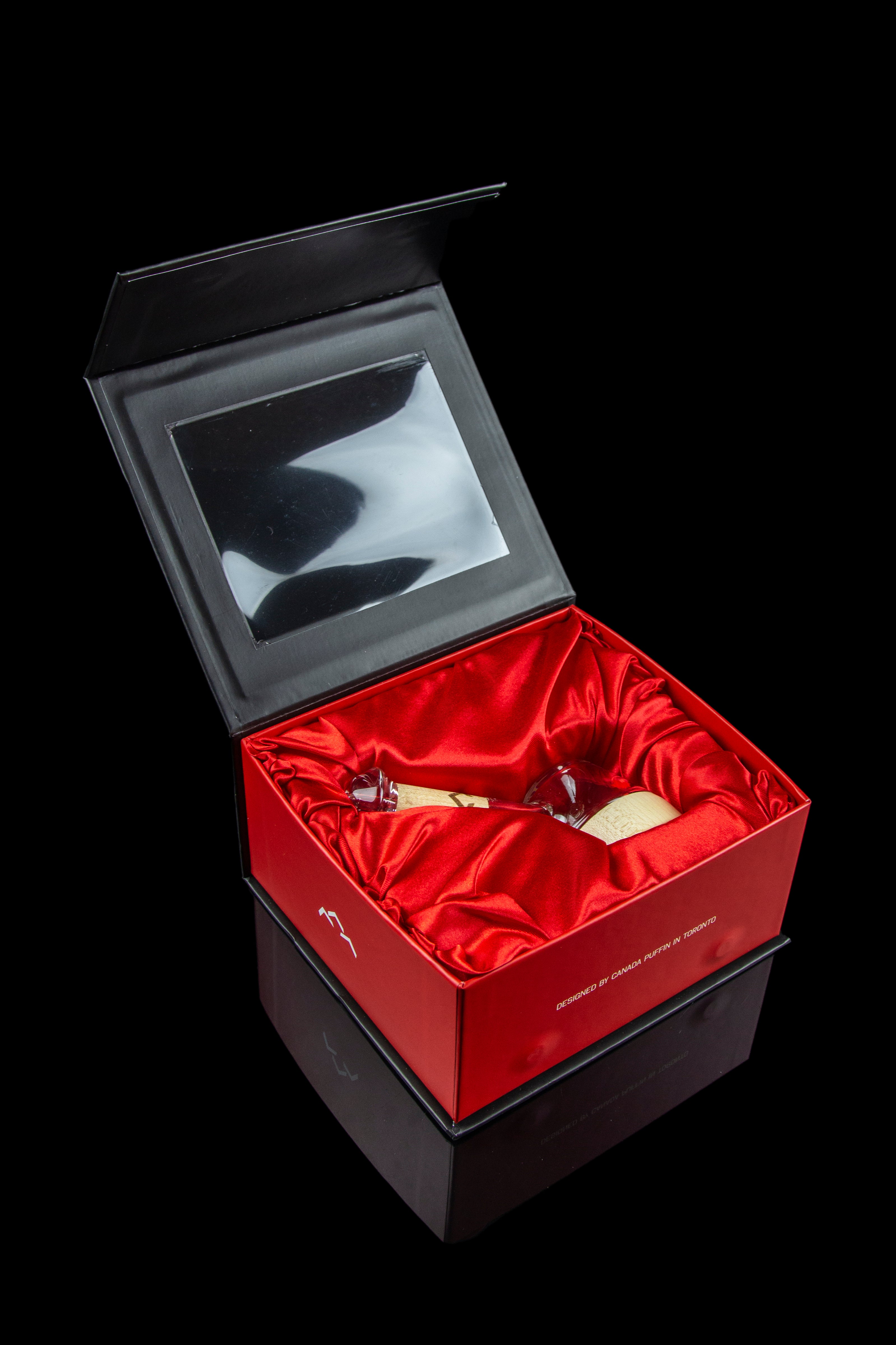 Luxurious red gift box with a glass cannabis oil rig inside, reflecting on a glossy black surface.