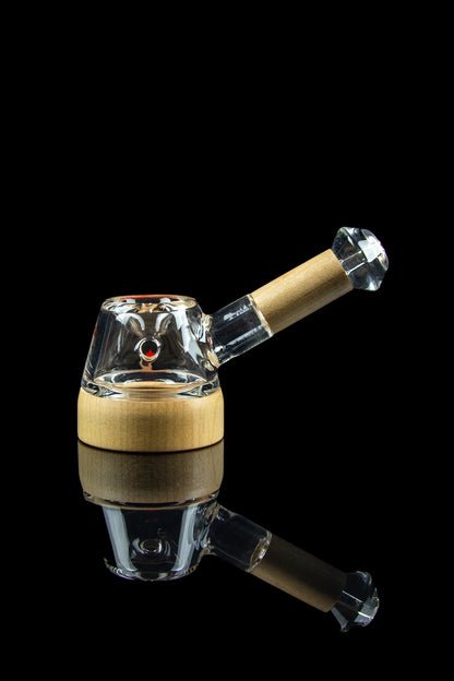 A glass bubbler pipe with a wood-grain patterned mouthpiece, displayed against a black reflective surface.