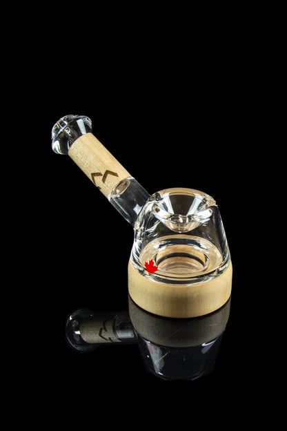 Glass bubbler with a maple leaf design, reflecting on a black surface.