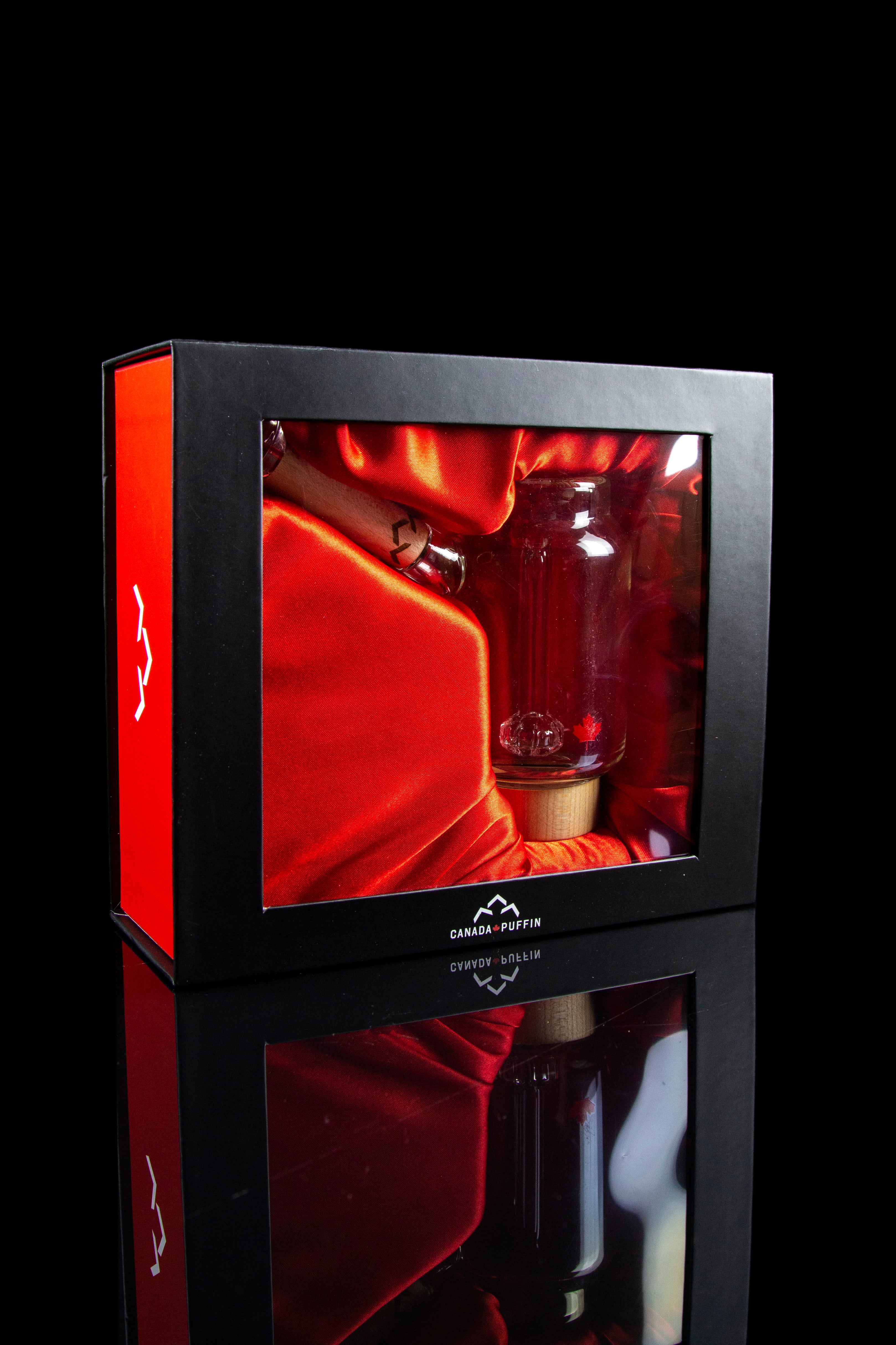 A sleek, red display box showcases a glass cannabis water pipe, reflecting on a glossy surface with “Canada Puffin” branding.
