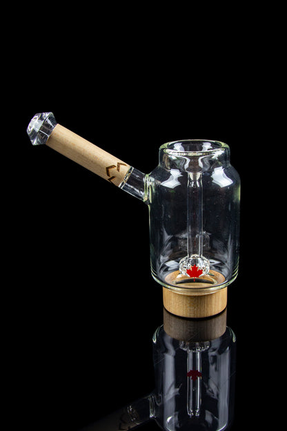 Clear glass bubbler with a wooden mouthpiece and red accent, reflecting on a glossy black surface.