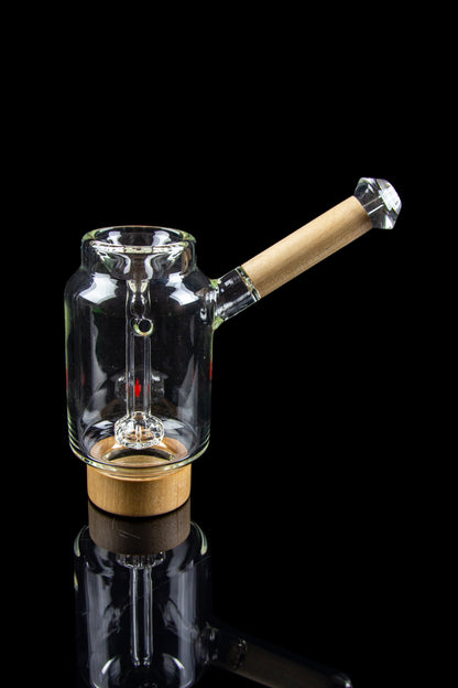 Glass water pipe with a wooden base and mouthpiece, studio shot on a black reflective surface.