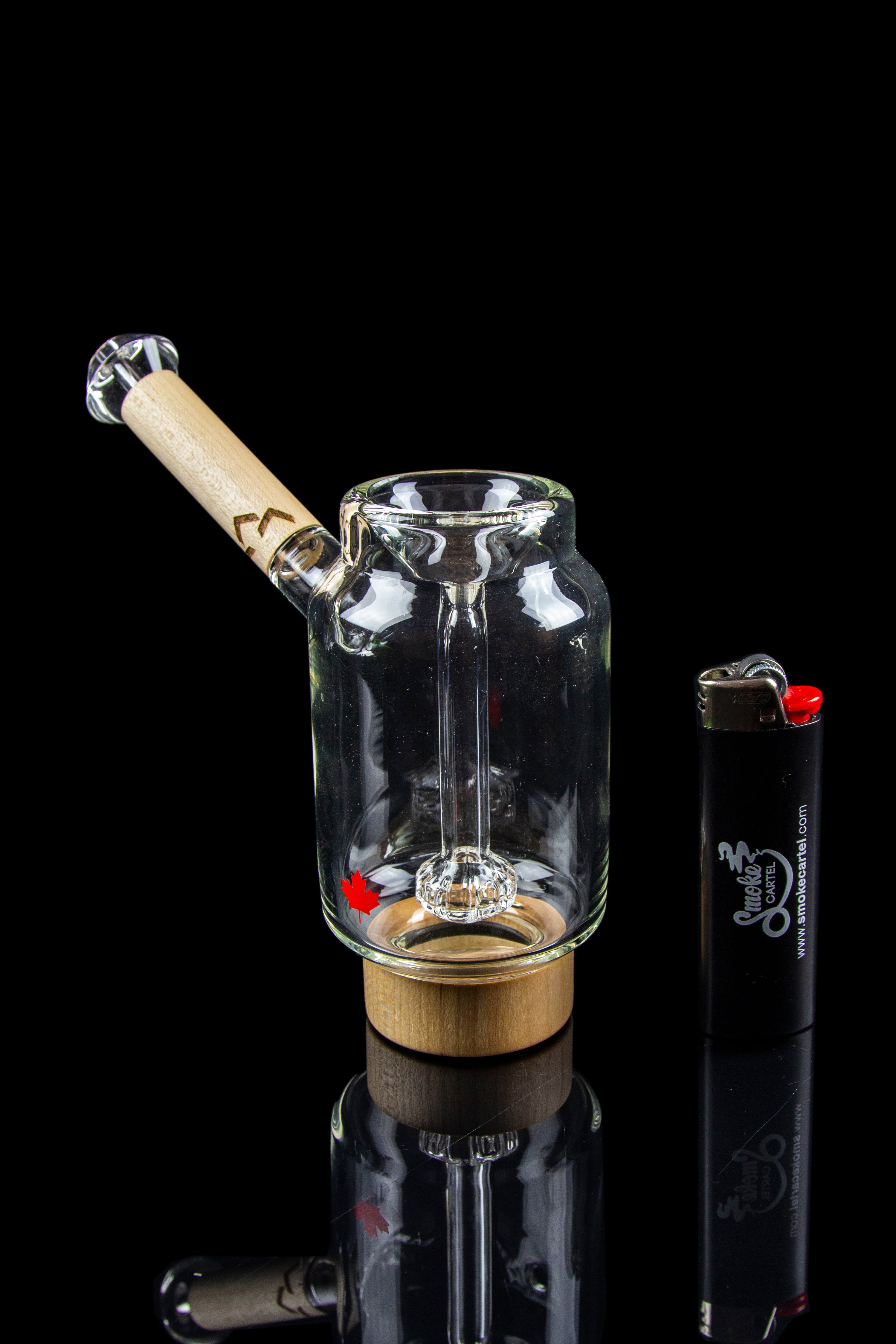 Glass water pipe with a wooden mouthpiece and quartz insert, displayed with a lighter on a reflective surface.
