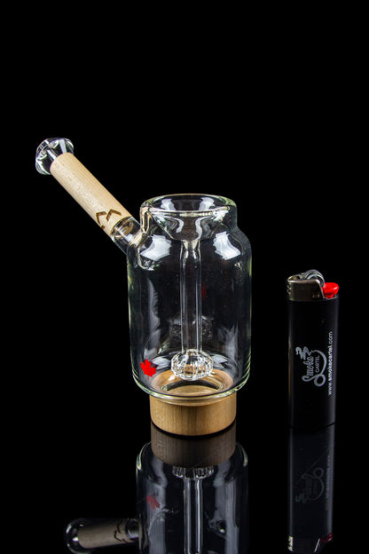 Glass water pipe with a wooden mouthpiece and quartz insert, displayed with a lighter on a reflective surface.