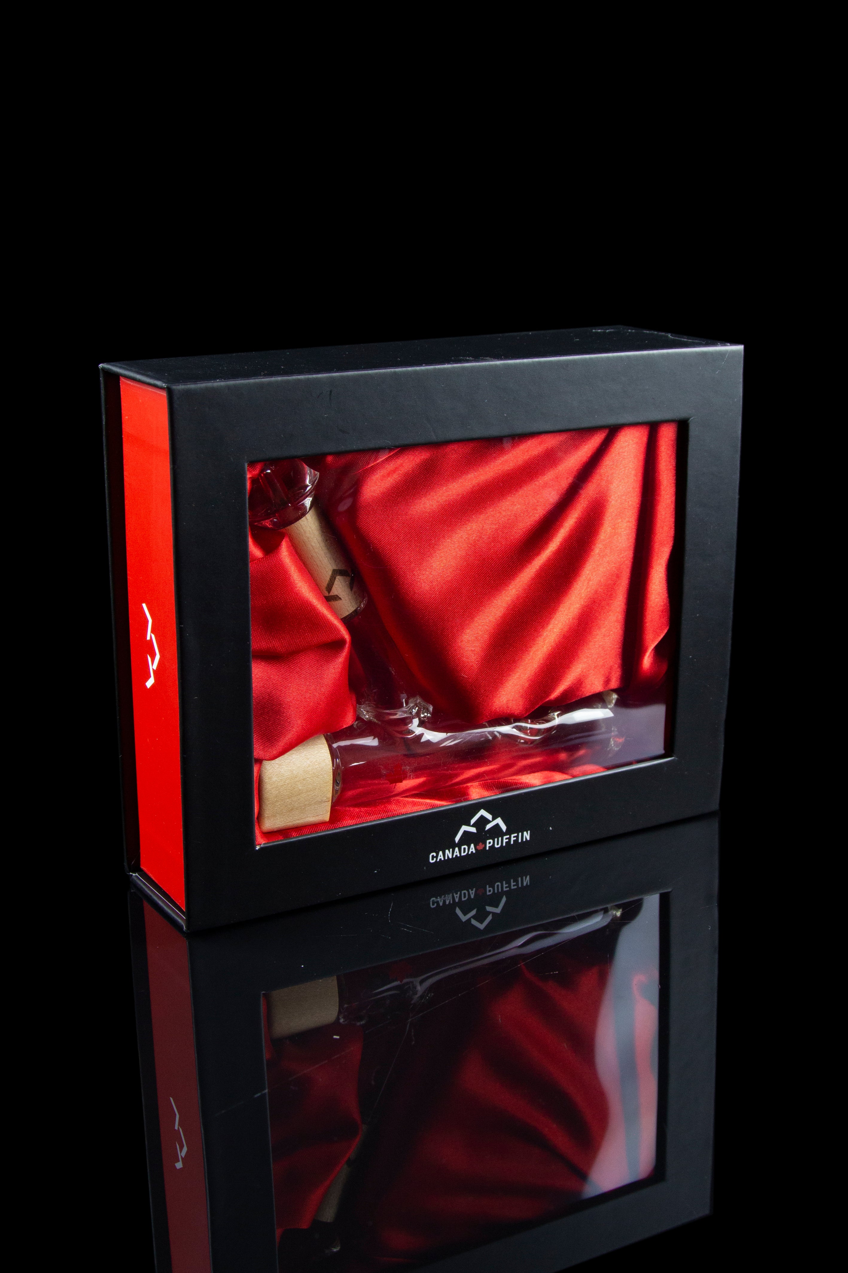 Red gift box containing a glass cannabis pipe on red silk, with branding for “Canada Puffin.” 