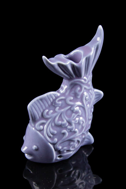 Lavender ceramic fish-shaped water pipe with detailed embossed floral patterns, isolated on a black surface.