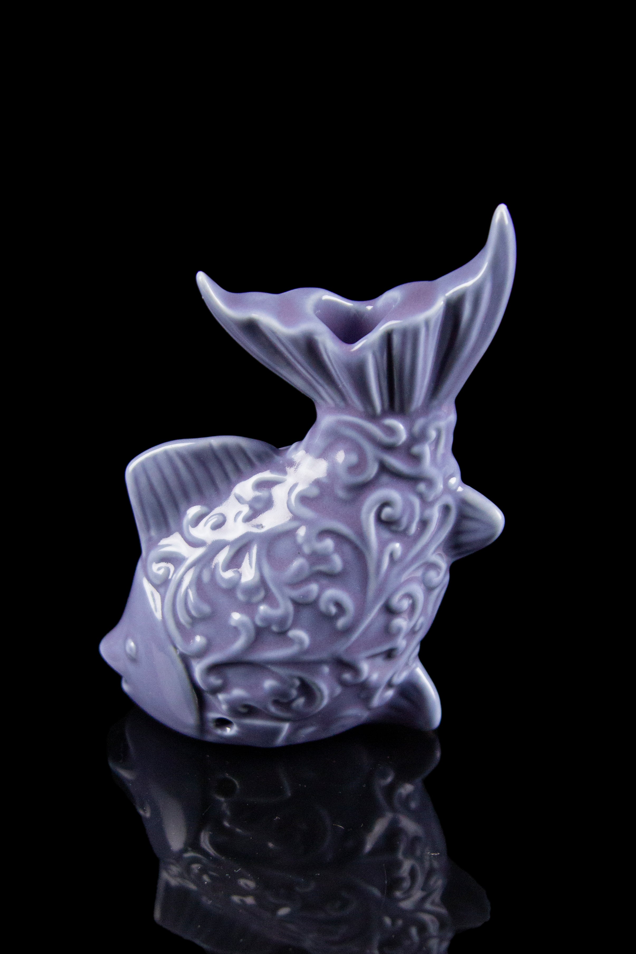 Purple ceramic pipe shaped like a whimsical seahorse with ornate detailing, reflected on a glossy black surface.