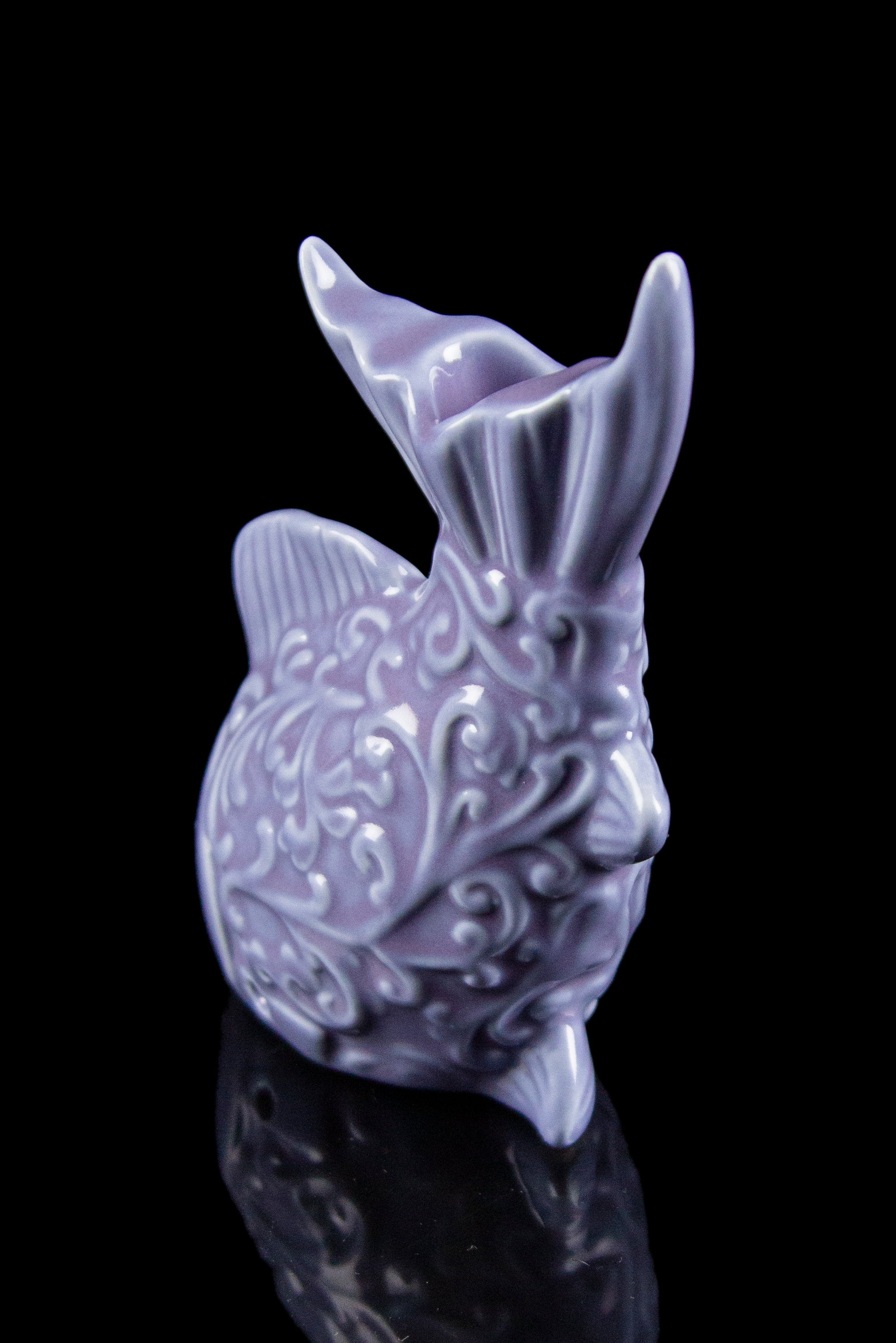 Lavender ceramic water pipe shaped like a bunny with ornate detailing, reflecting on a dark surface.