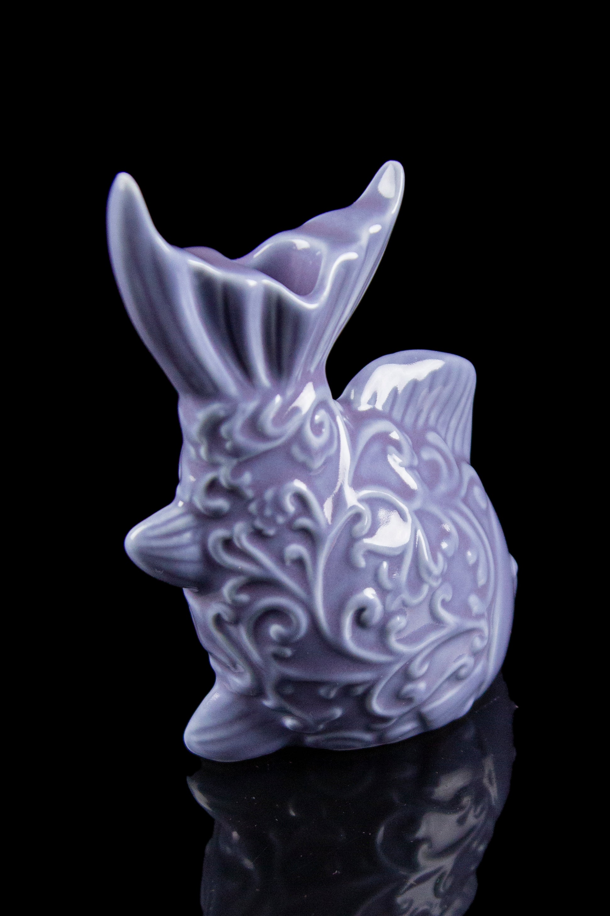 Purple ceramic pipe shaped like a pufferfish, detailed with swirling patterns, displayed on a reflective surface.