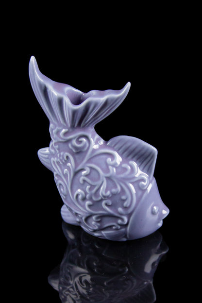 Purple ceramic fish-shaped water pipe with ornate detailing, reflecting on a glossy black surface.
