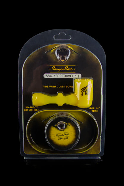 A clear, sealed travel kit containing a glass pipe with bowl, grinder, and rolling tray, branded with "Honeybee Herbs."