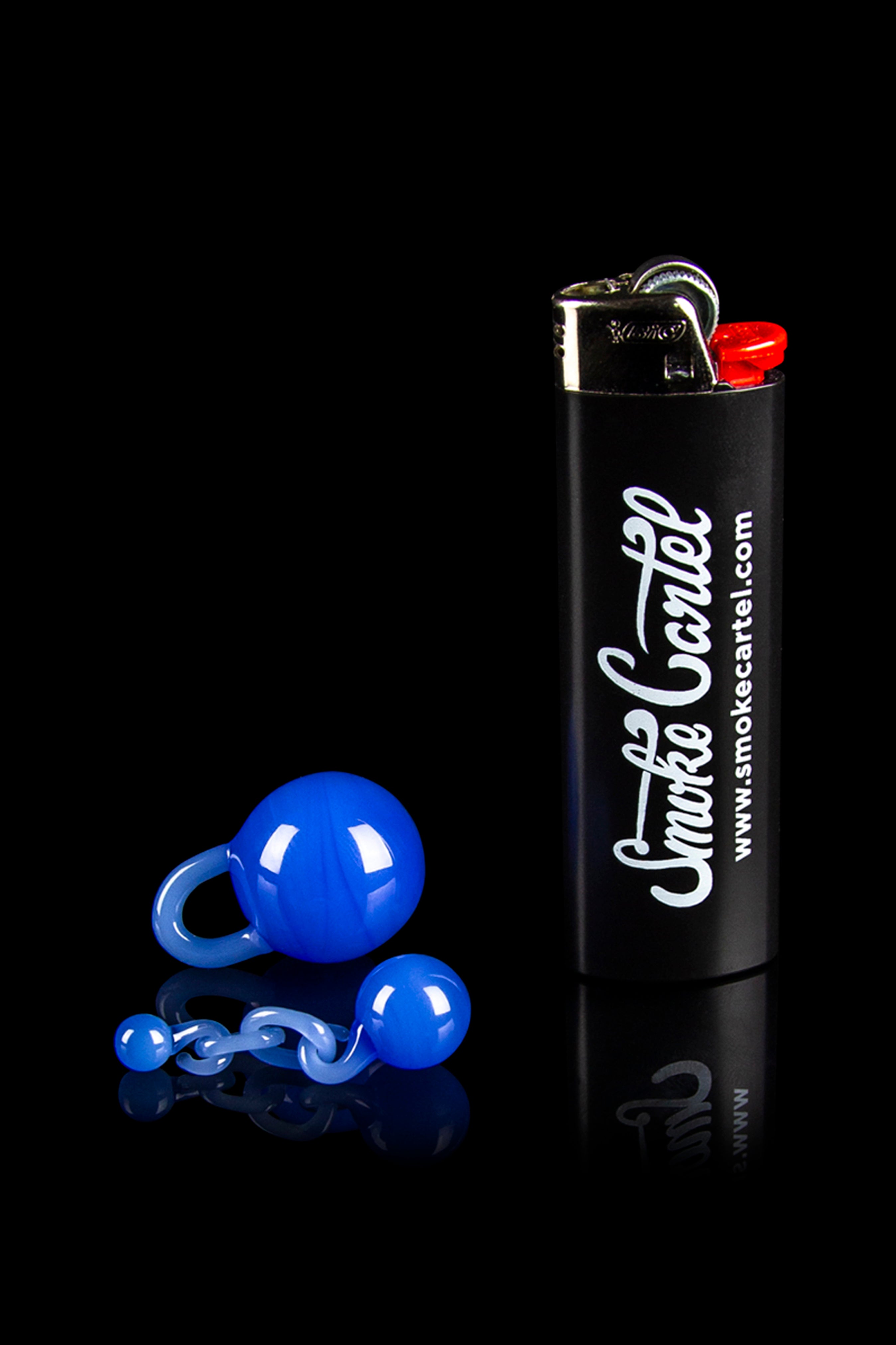Blue glass marbles and a black lighter with “Smoke Cartel” branding on a reflective surface.