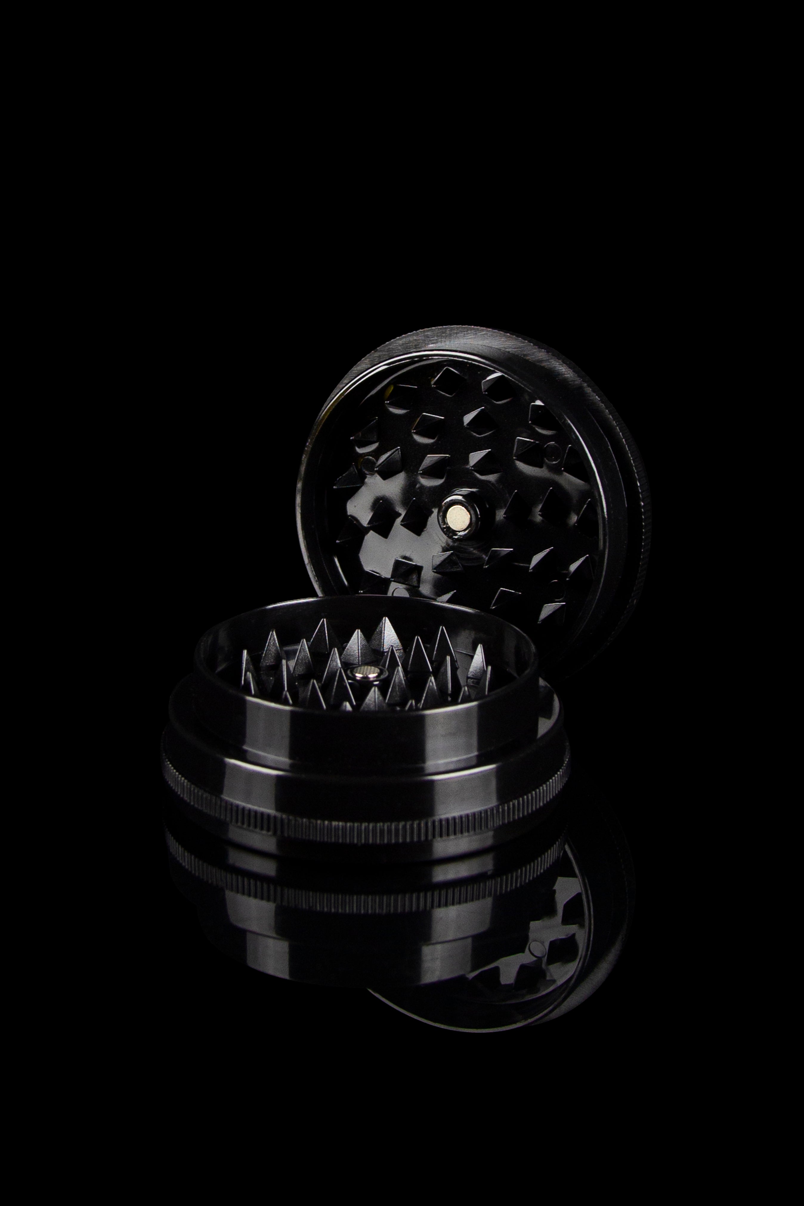 Black metal cannabis grinder disassembled, revealing tiered grinding components.