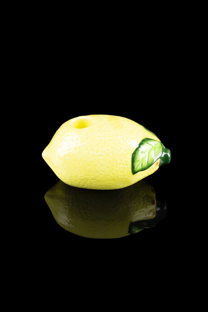 Yellow lemon-shaped glass pipe with a green leaf detail, reflecting on a black surface."