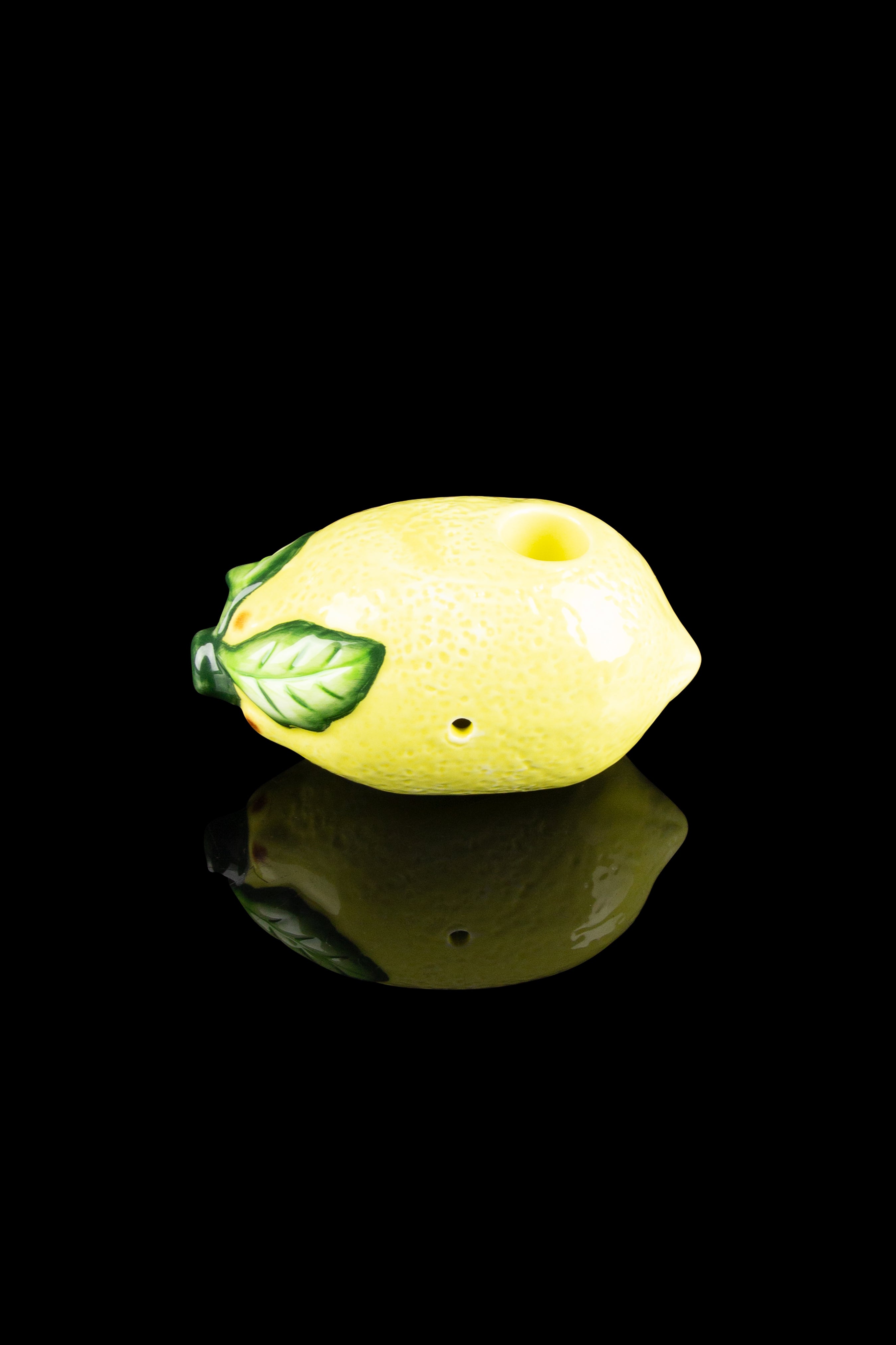 Lemon-shaped glass pipe with a green leaf detail, reflecting on a dark surface.