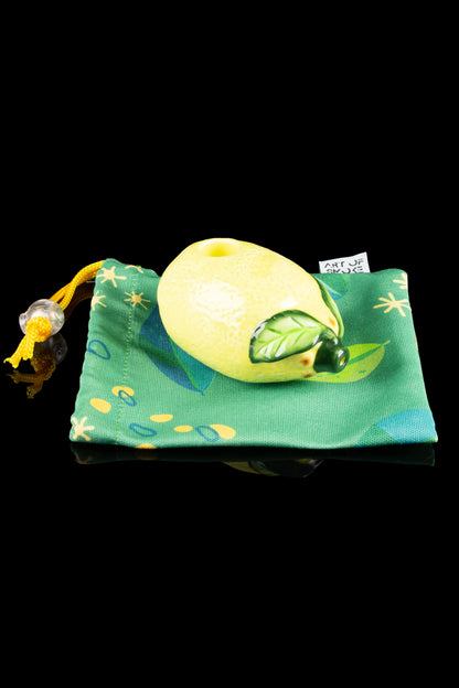 A bright green cannabis-themed velvet pouch with a yellow drawstring and a small cannabis bud-shaped charm, resting on a dark surface.