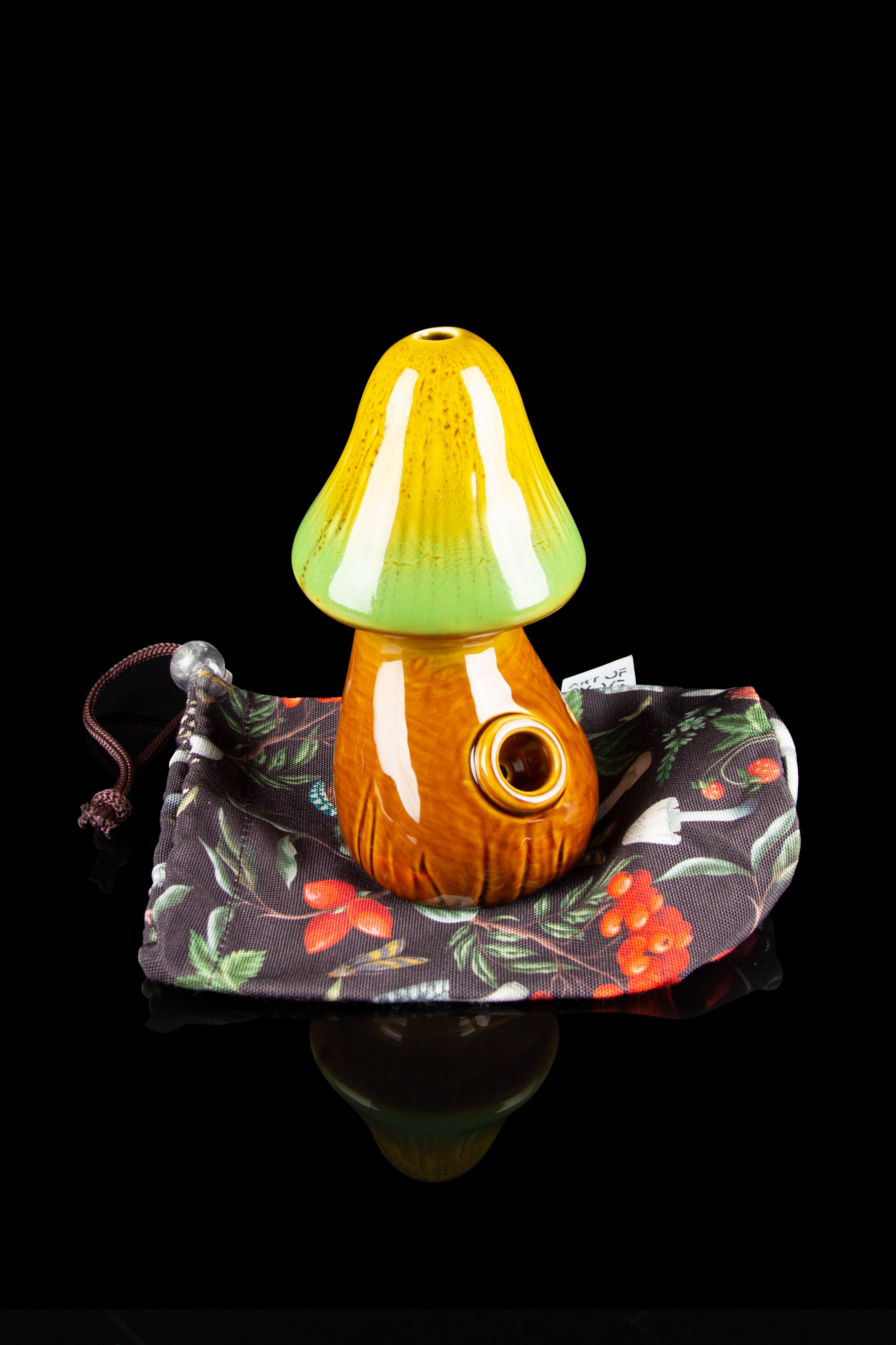 Ceramic mushroom-shaped pipe resting in a floral patterned pouch, reflected on a glossy black surface.