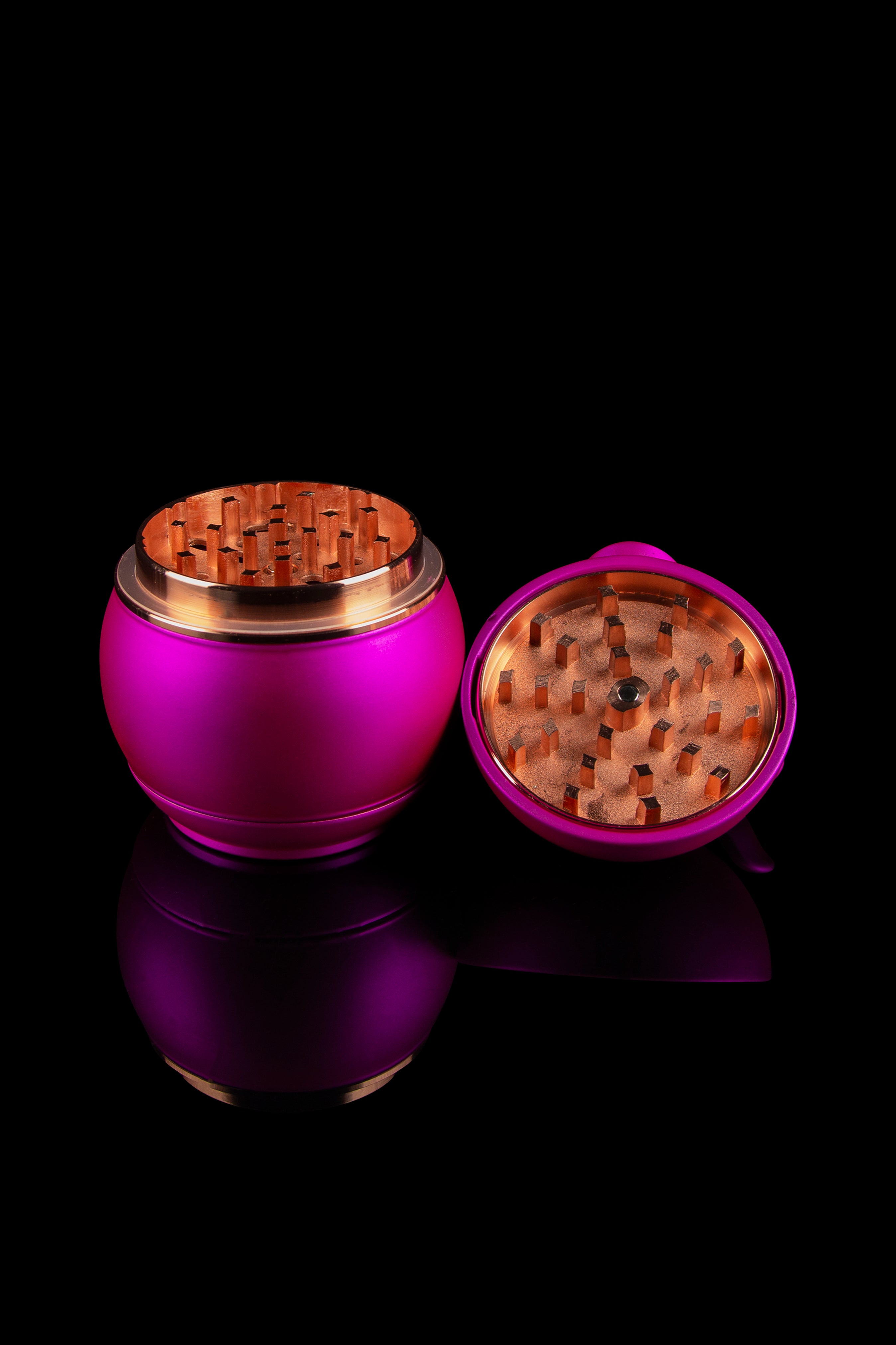 Open pink cannabis grinder with gold accents, reflecting on a dark surface."