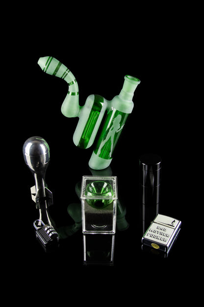 Green glass cannabis rig with accompanying accessories displayed on a reflective black surface.