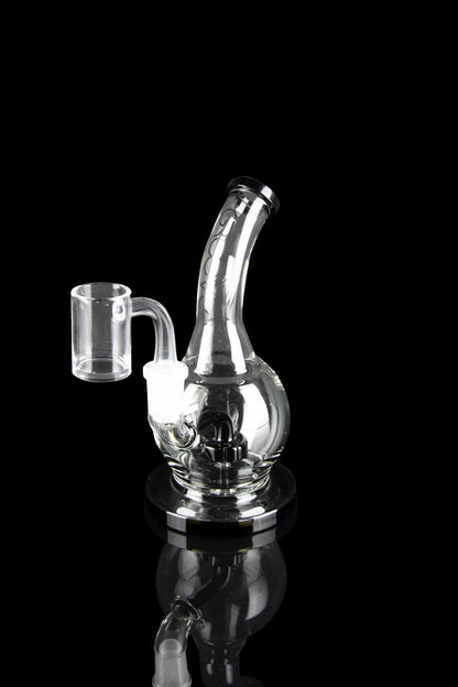 Clear glass dab rig with a quartz banger, reflecting on a black surface.