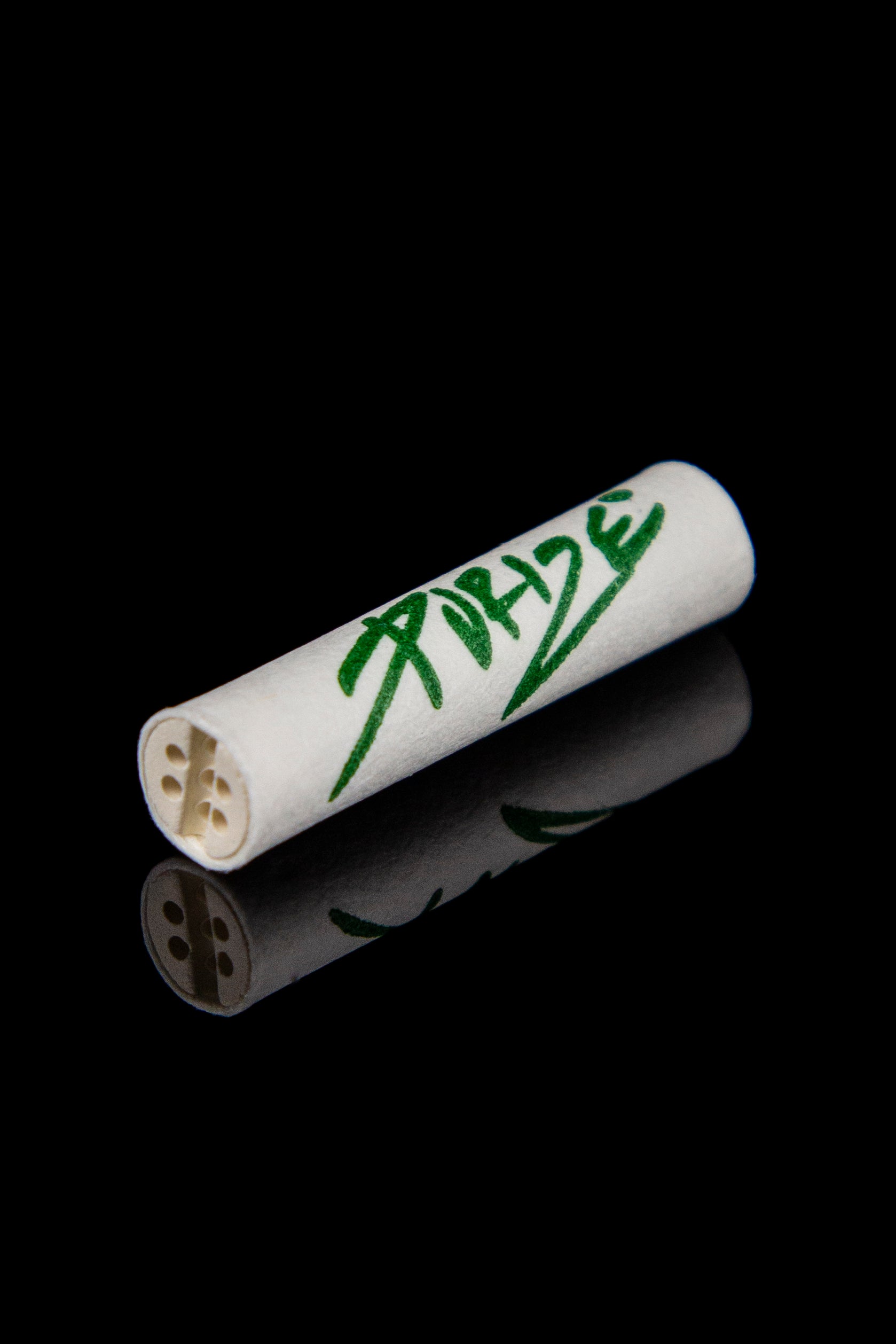White cannabis filter tip with green handwritten text and floral design, reflecting on a black surface.