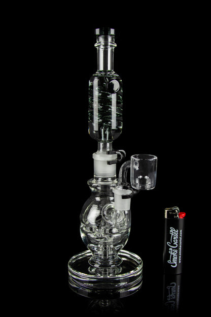 Clear glass water pipe (rig) with a quartz banger, displayed on a reflective surface.