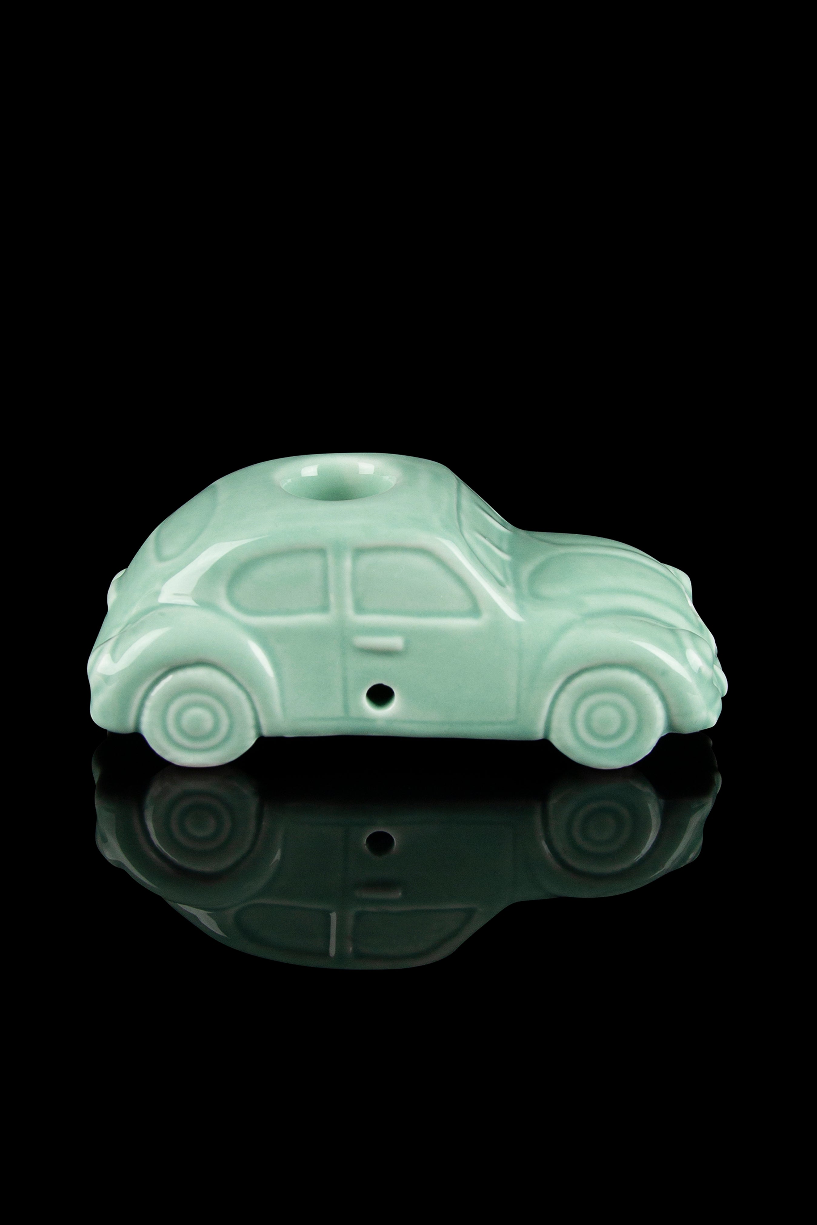 Pale green ceramic car-shaped pipe with a glossy reflection on a black surface.
