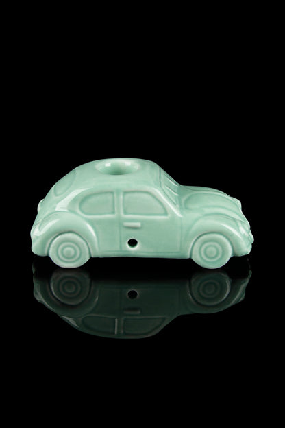 Pale green ceramic car-shaped pipe with a glossy reflection on a black surface.