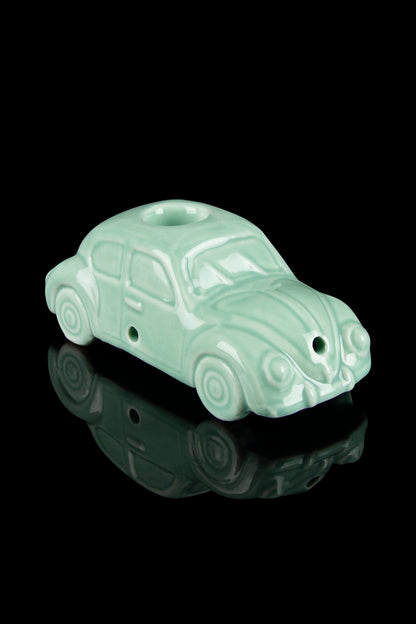 Mint green Volkswagen Beetle-shaped glass pipe with a glossy reflection on a black surface.
