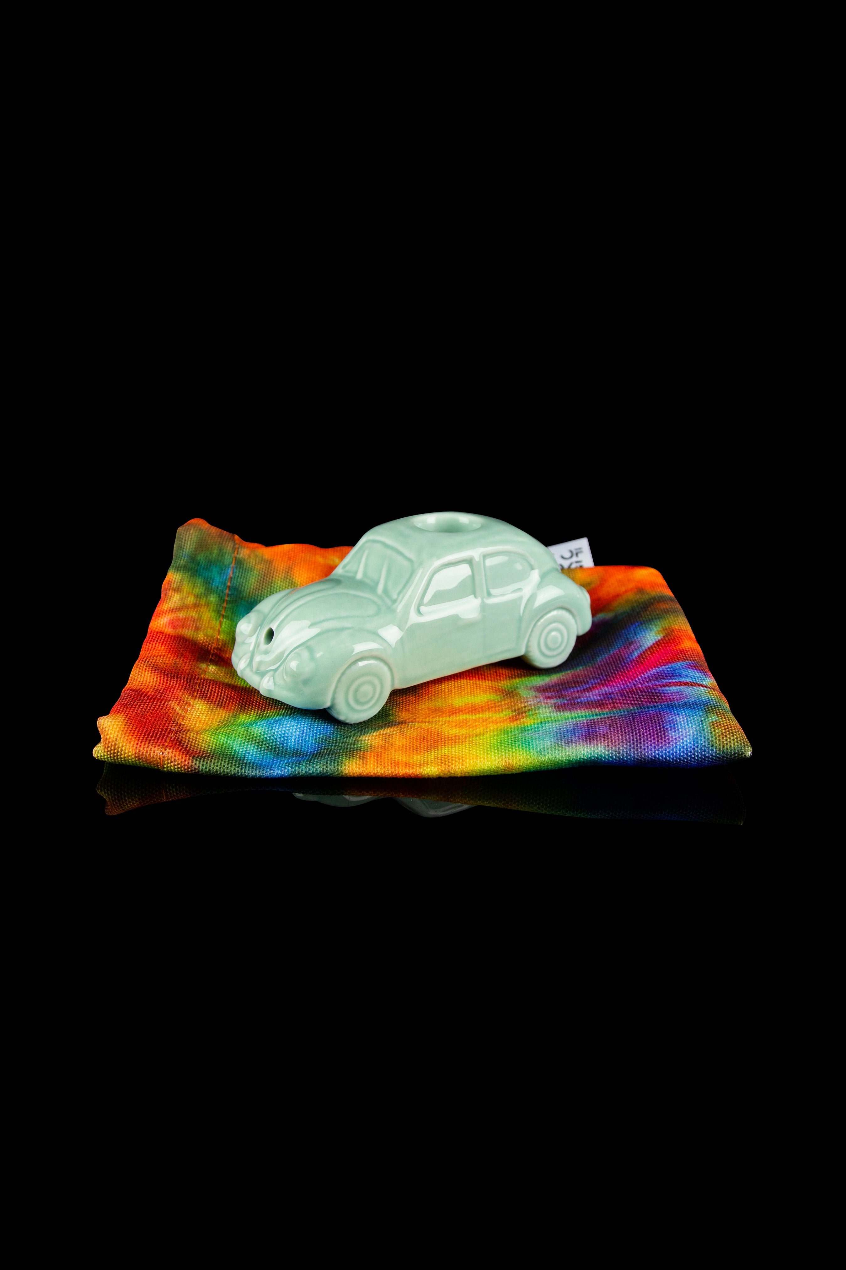 Green glass car-shaped smoking piece rests on a tie-dye patterned bag.