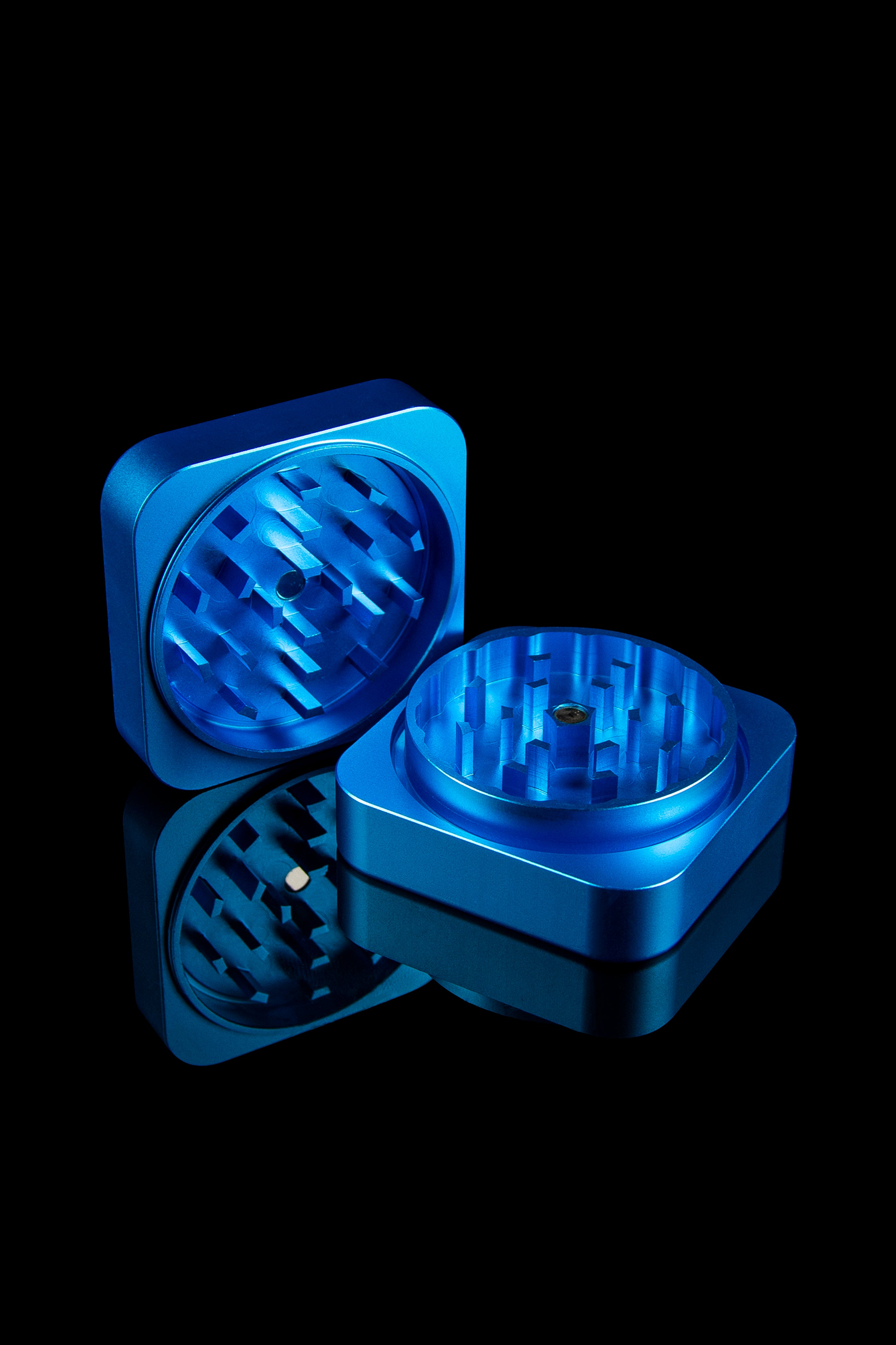 Blue metal cannabis grinder, open with visible grinding teeth, against a black background.