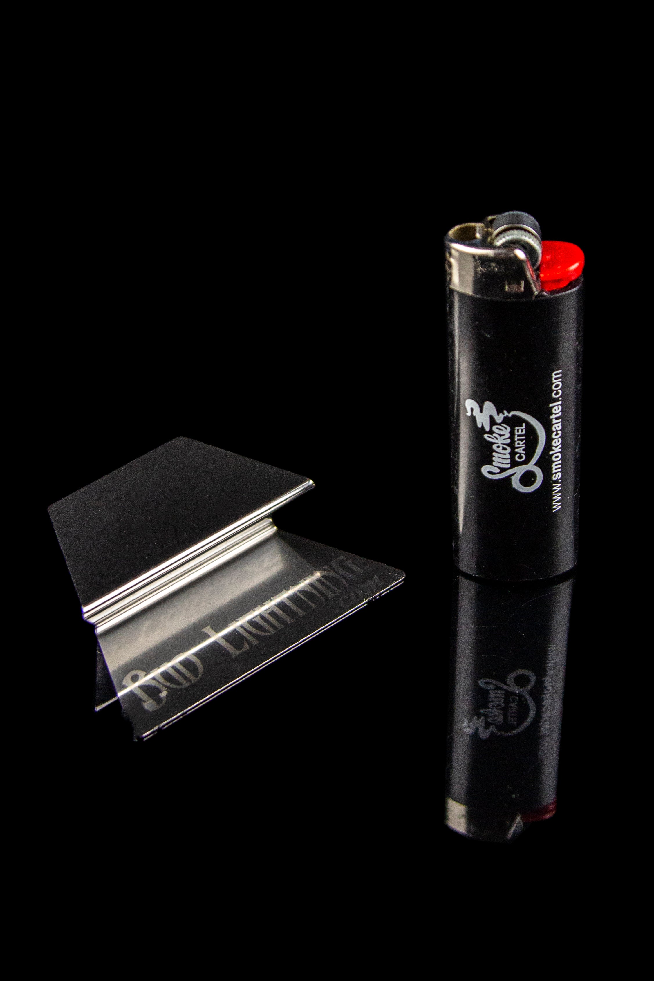 Metal rolling papers and a black lighter with “Smoke Cartel” branding against a dark background.