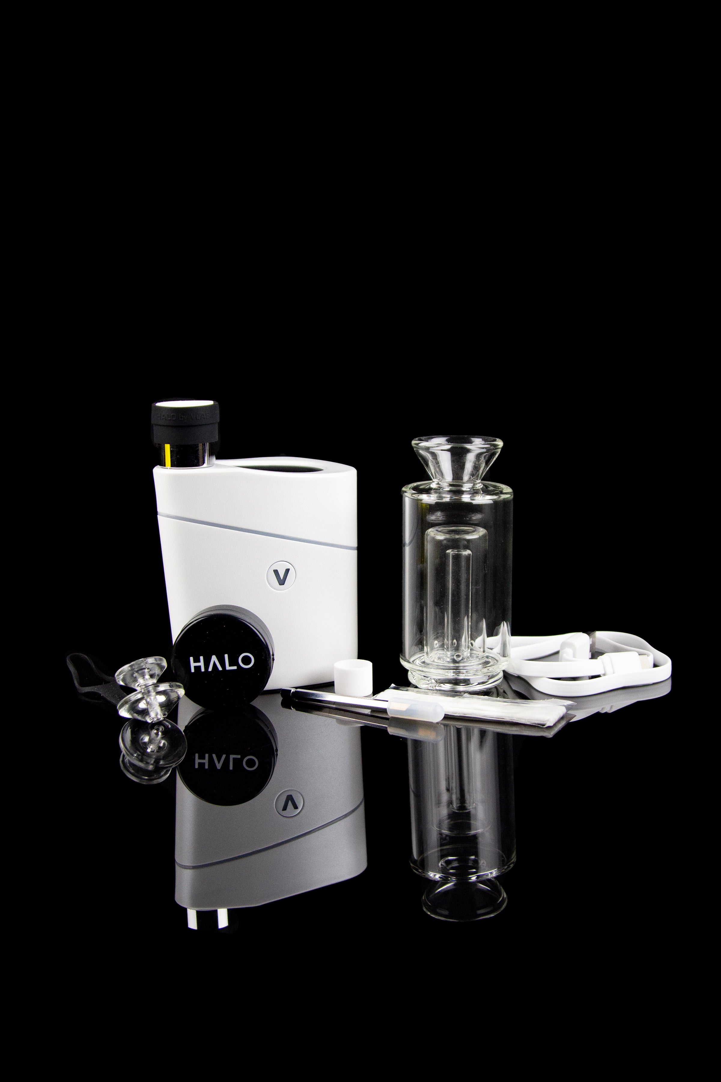 White and grey cannabis vaporizer with glass attachment and accessories on a reflective surface.
