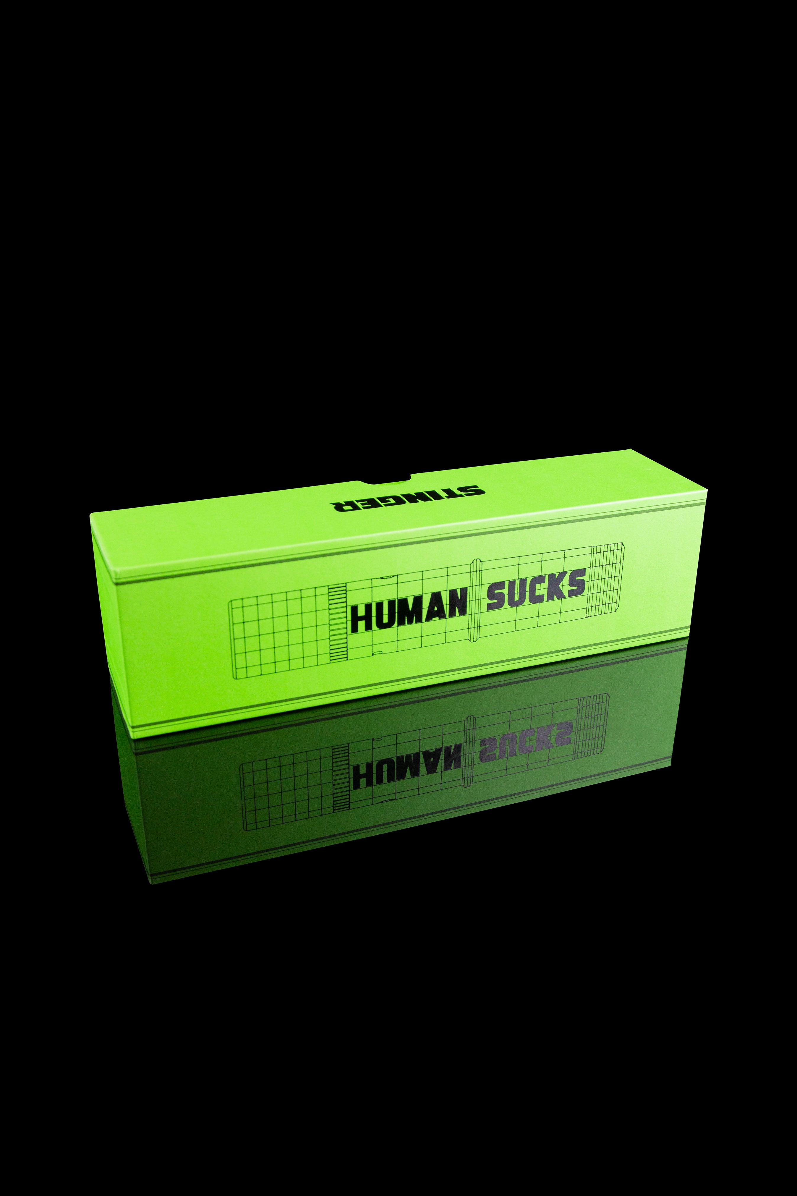 Neon green cannabis storage box with “HUMAN SUCKS” text in pink, reflected on a black surface.