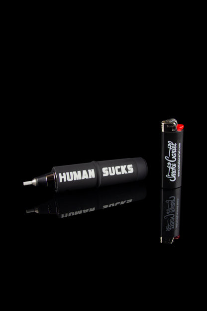 Black cannabis pipe and accessories with bold white and red text reading "HUMAN SUCKS" and a lighter beside it, against a black background.