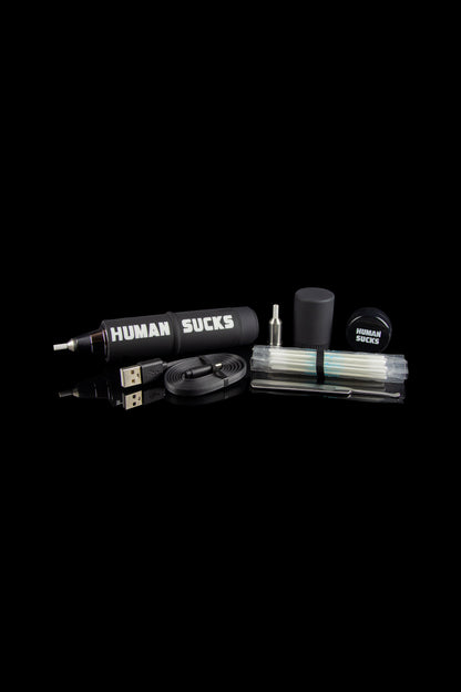 Cannabis vaping kit with pen, charger, and accessories on a black background, branded with “HUMAN SUCKS.”