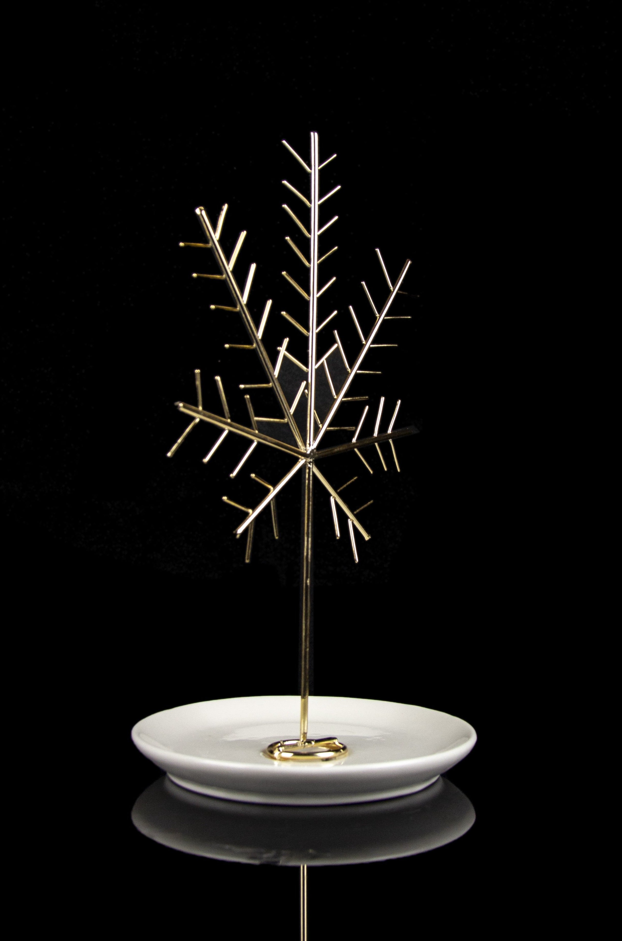 Gold cannabis oil burner with intricate branching design on a white dish, reflecting on a black surface.