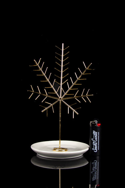 Gold cannabis leaf-shaped oil burner rig with a white dish, reflecting on a glossy black surface.