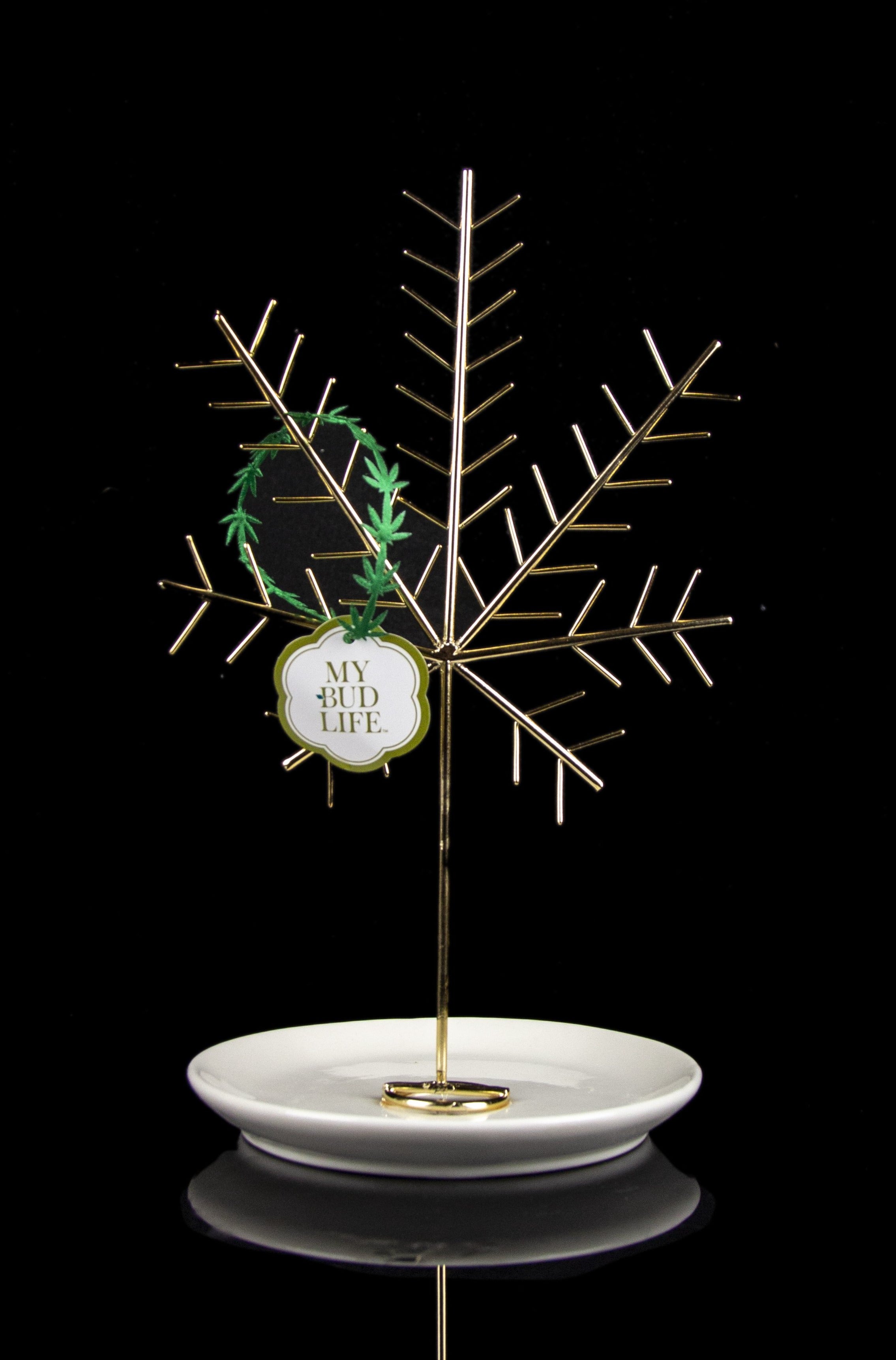 Gold cannabis display stand with a small sprig of green cannabis and a tag reading "My Bud Life" resting on a white dish.
