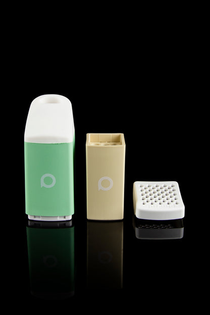 Puffco Peak cannabis concentrate vaporizer components—a green atomizer, yellow heating element, and white extraction tool—displayed on a reflective black surface.