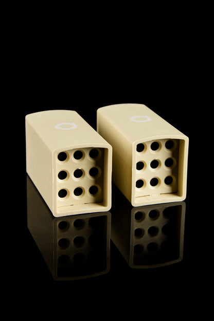 Two cream-colored one-hitters with perforated bowls rest on a reflective black surface.
