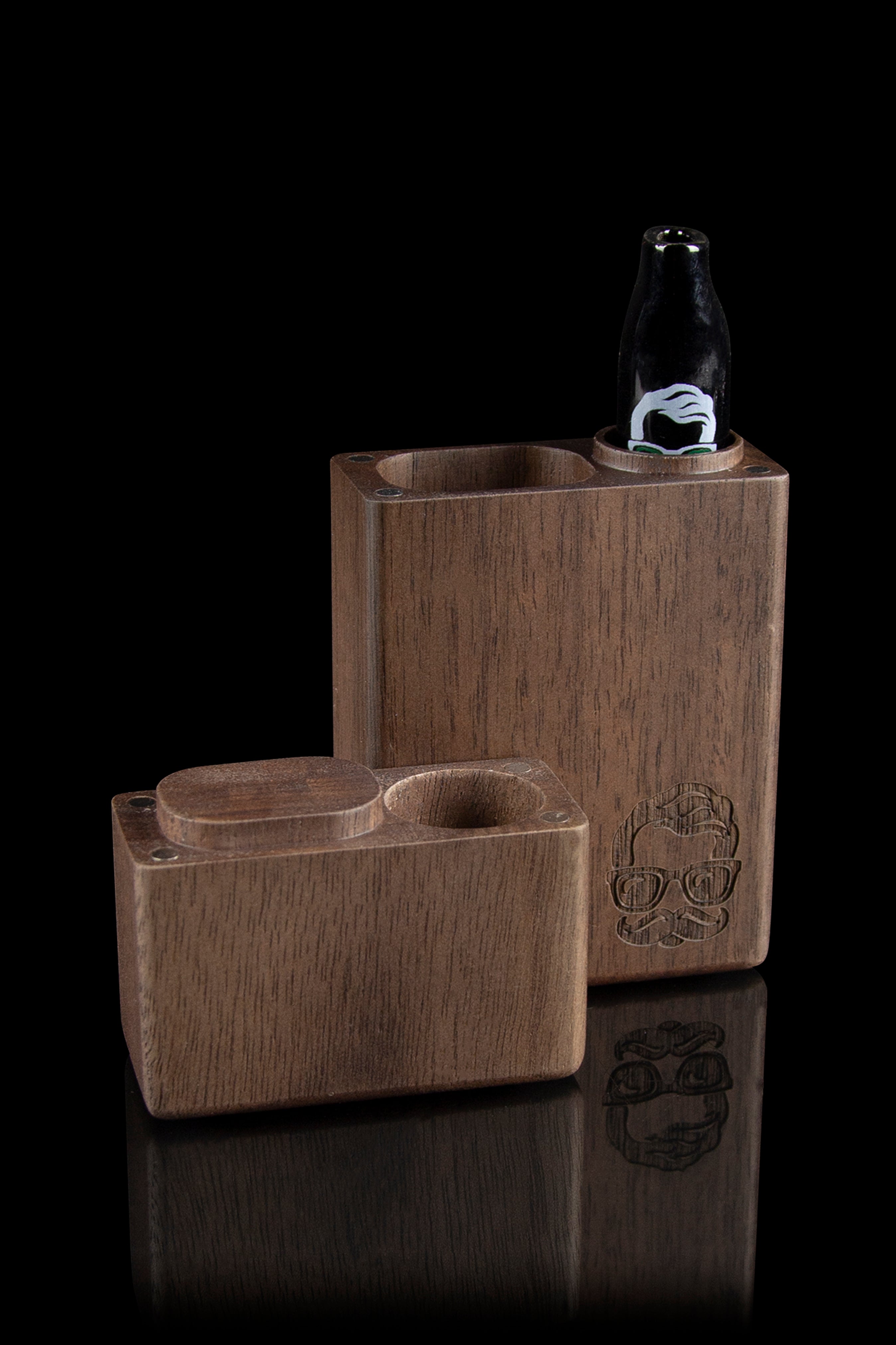 Wooden cannabis pipe and storage box with skull carving, reflected on a glossy surface.