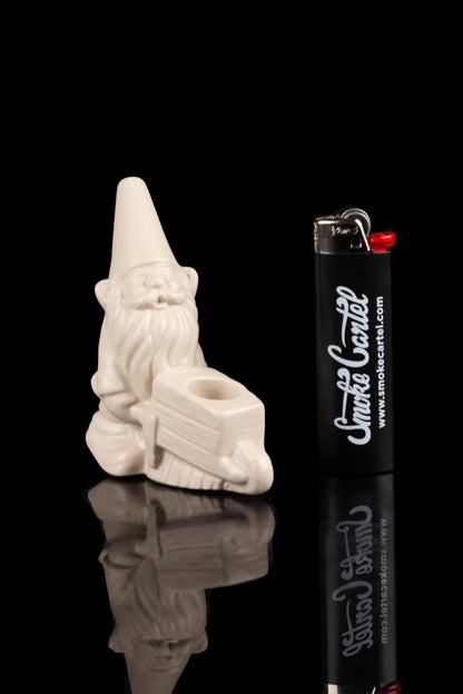 White glass cannabis water pipe with a skull design, displayed next to a black “Smoke Cartel” branded lighter on a reflective surface.