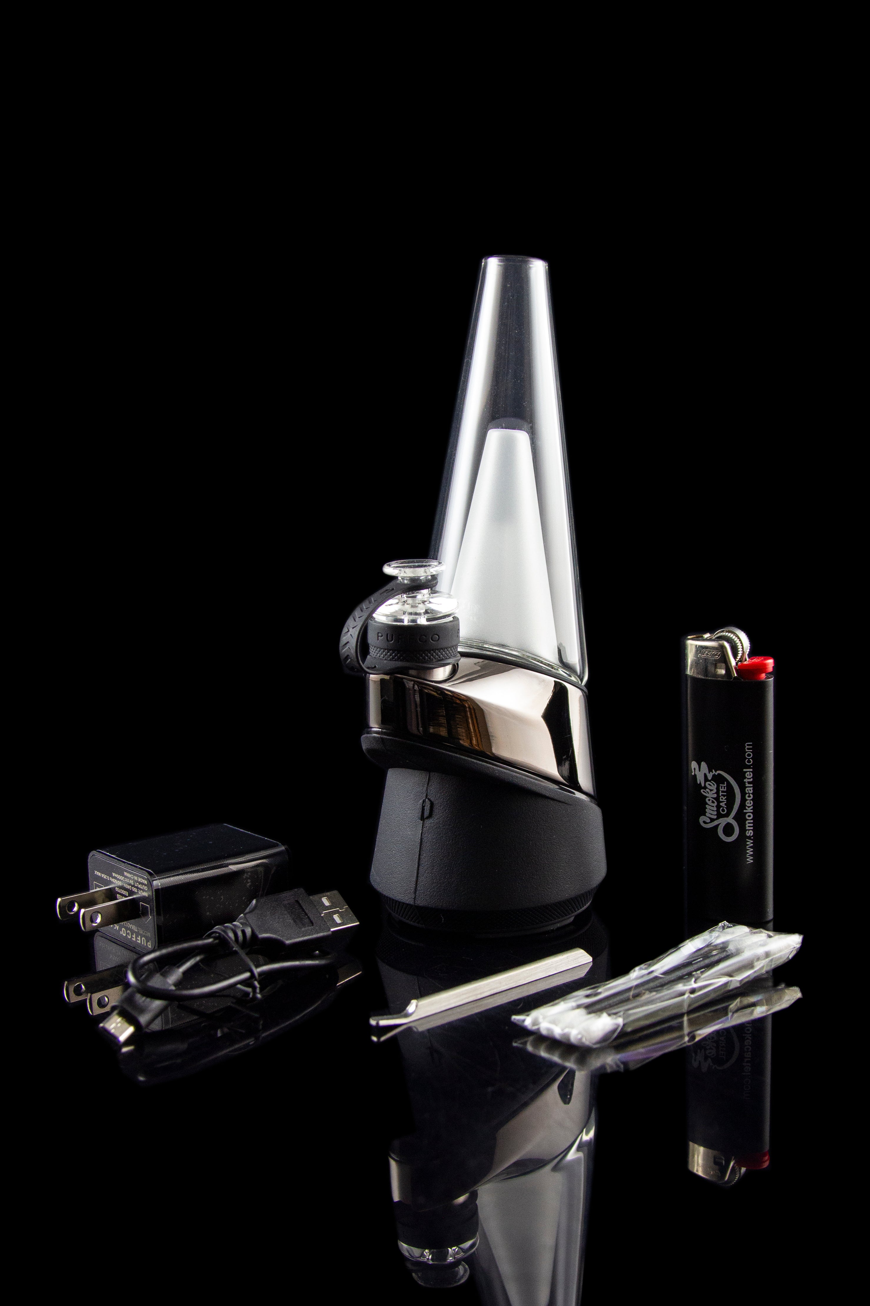 Black Peak cannabis e-rig with accessories, including a lighter, charging plug, and dab tool, displayed on a reflective surface.