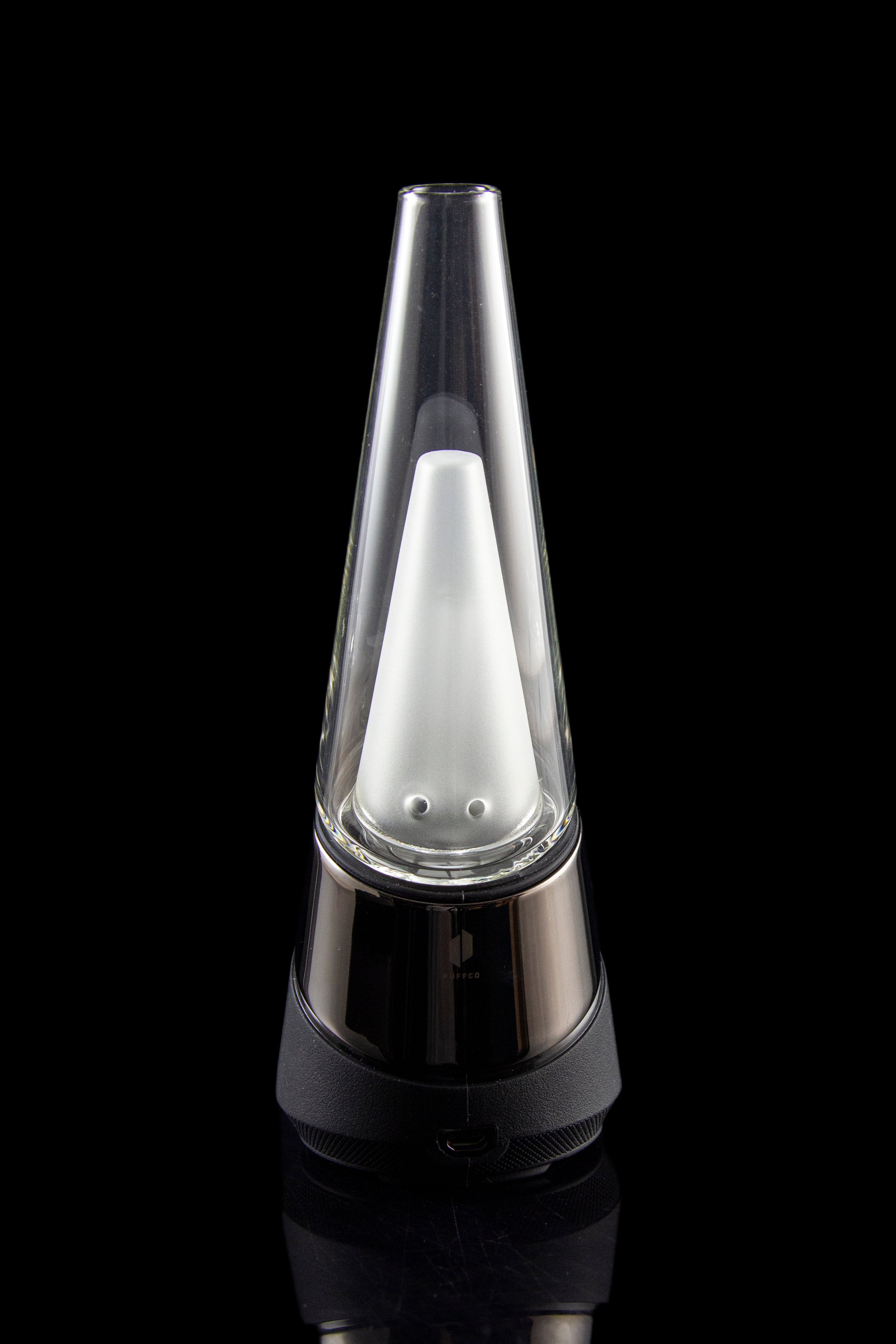 A Peak portable cannabis vaporizer with a glass mouthpiece emitting a visible vapor cloud, set against a black background.