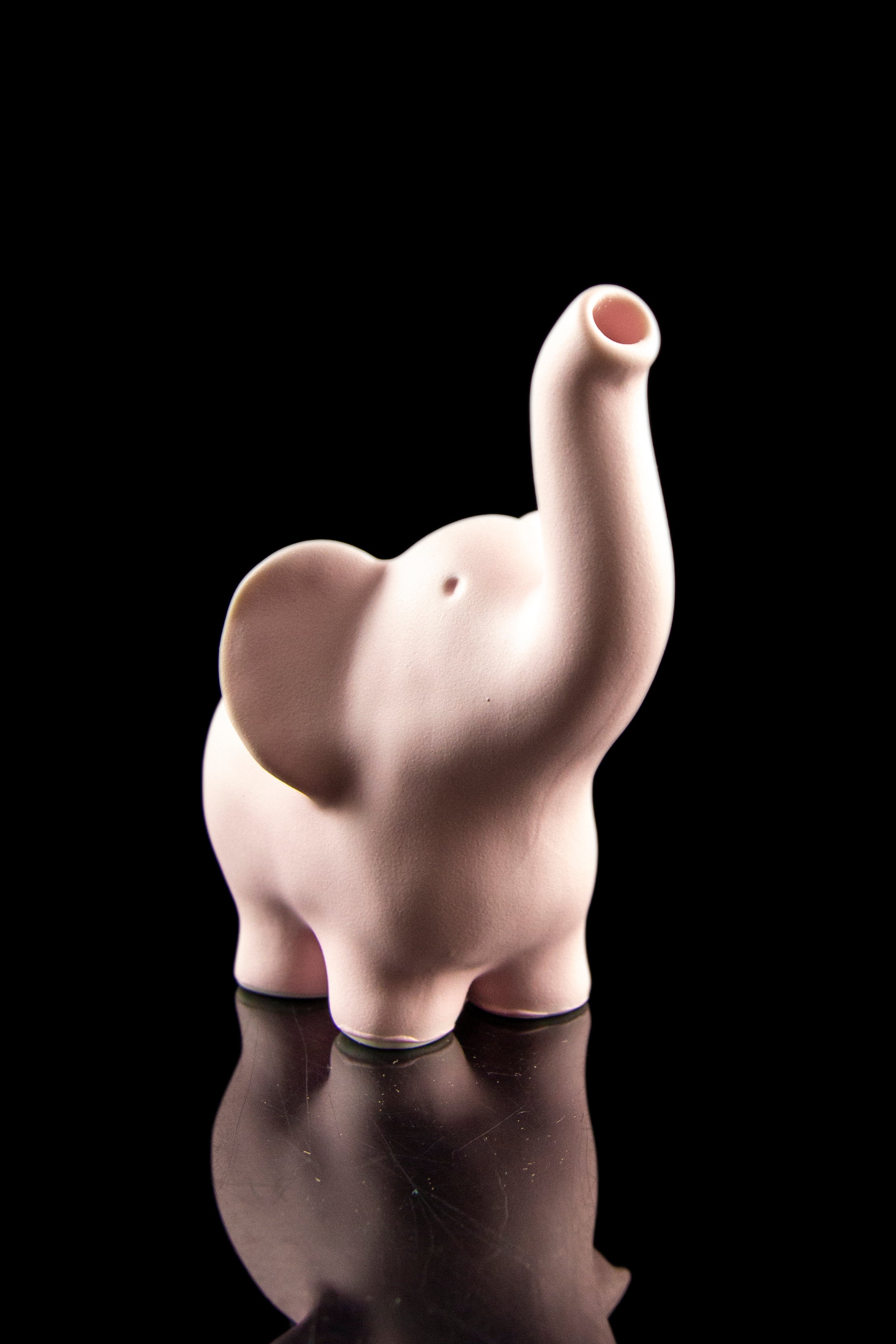 Pink ceramic elephant water pipe with a glossy finish, reflected on a dark surface.