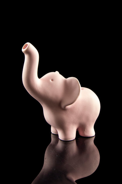 Pink ceramic elephant-shaped water pipe with a raised trunk, reflected on a black surface.