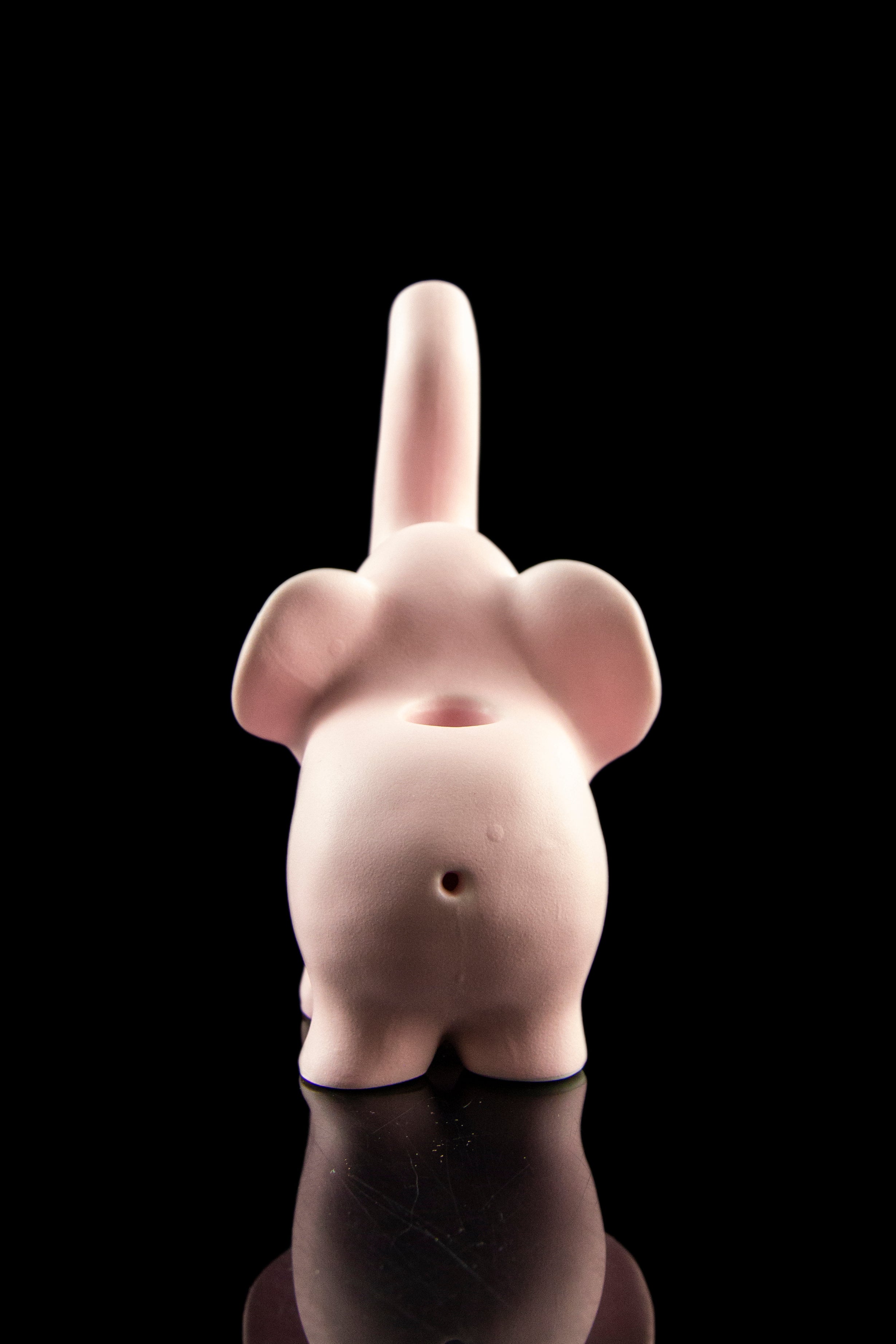 Pink ceramic pipe shaped like a bottom with a raised middle finger, reflected on a dark surface.